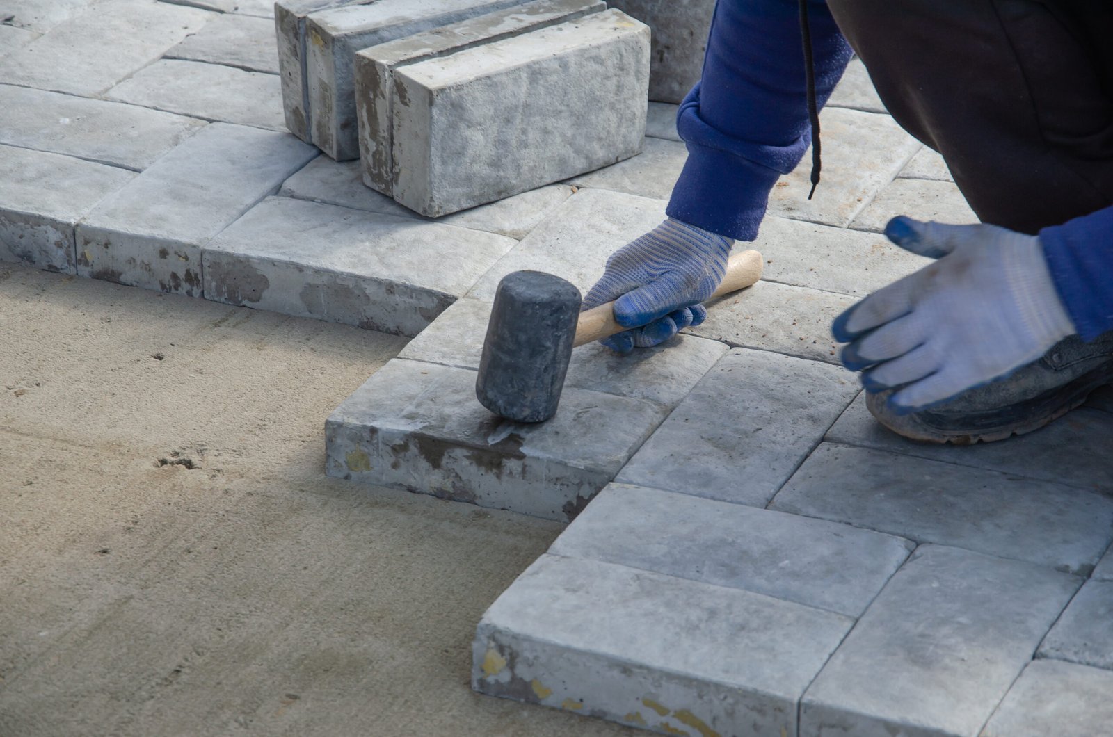 Construction of pavement near the house. Bricklayer places concrete paving stone blocks for building up a Sidewalk pavement Construction of pavement near the house. Bricklayer places concrete paving stone blocks for building up a