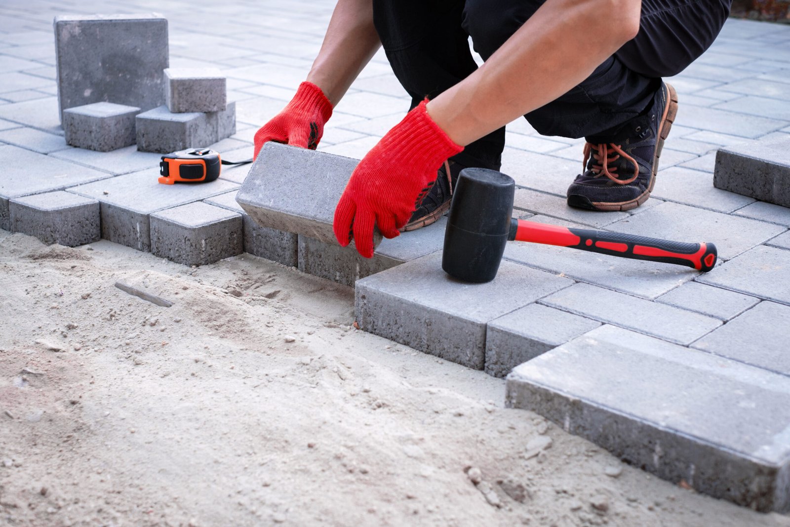 The master in yellow gloves lays paving stones The master in yellow gloves lays paving stones in layers. Garden brick pathway paving by professional paver worker. Laying gray concrete paving slabs in house courtyard on sand foundation base.