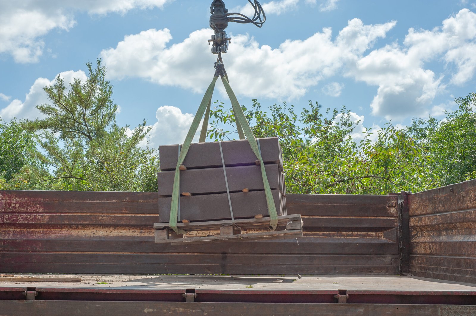 Unloading paving slabs from a truck. Men unload paving slabs using a manipulator. Workers unload building materials from a large machine. Unloading paving slabs from a truck. Men unload paving slabs using a manipulator.